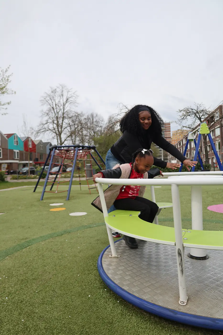 Buddy duwt een lachend meisje op de draaischijf van een speelplein in de buurt